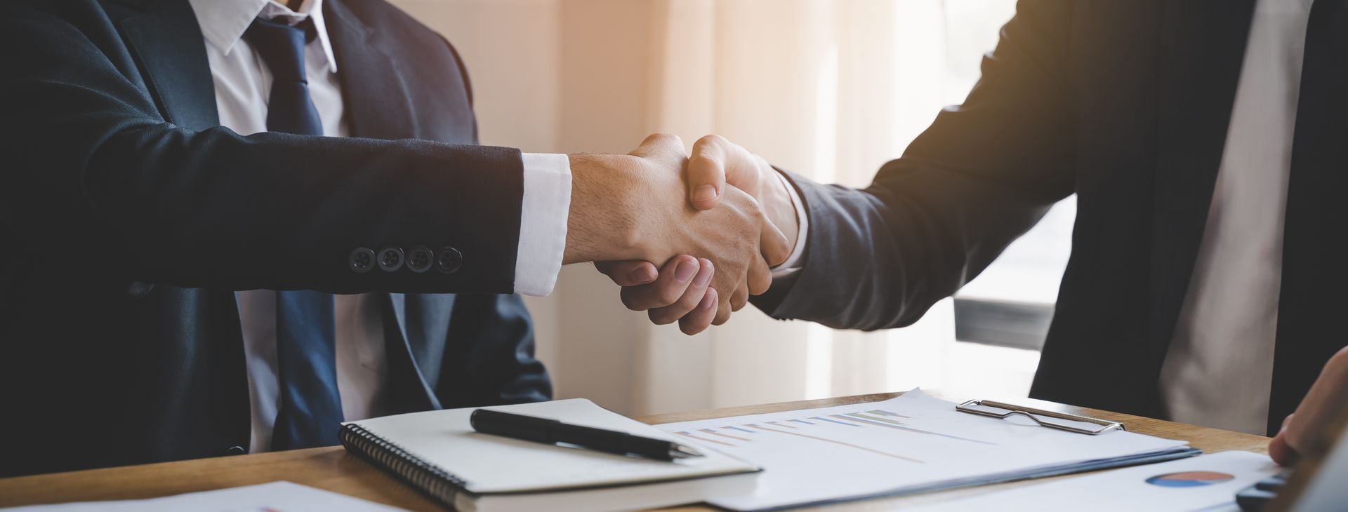 Two business people shaking hands over a contract on a table.