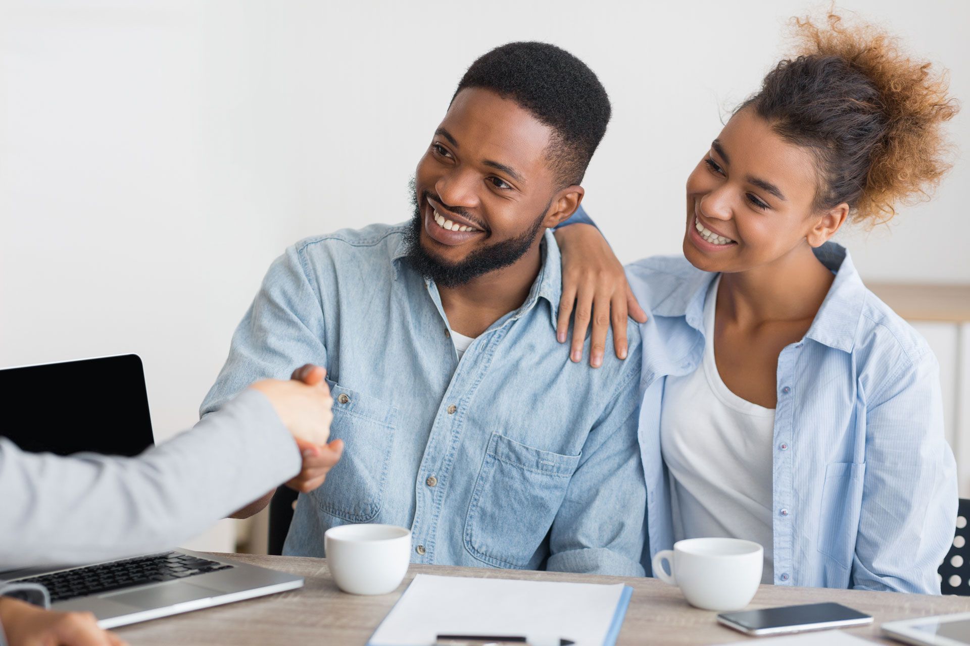 Couple smiles as they shake hands with a person at a table, likely finalizing a deal.
