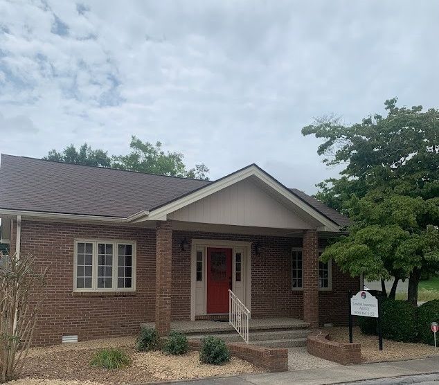 Brick building with red door, brown roof, and small sign on a cloudy day.