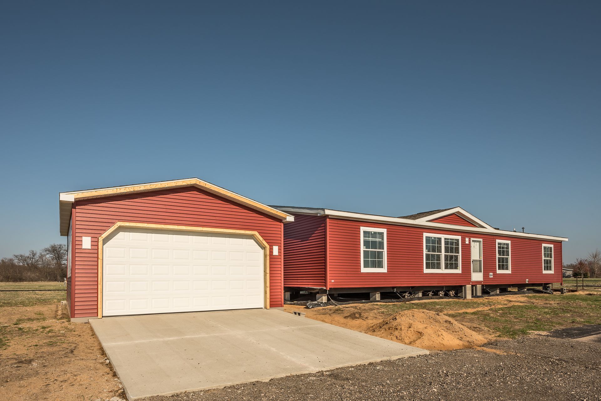 Red house with attached garage; concrete driveway under a clear blue sky.