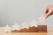 Hand placing a wooden star on a staircase of wooden blocks, indicating rating progress.