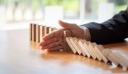 Hand stopping a row of falling dominoes on a table.