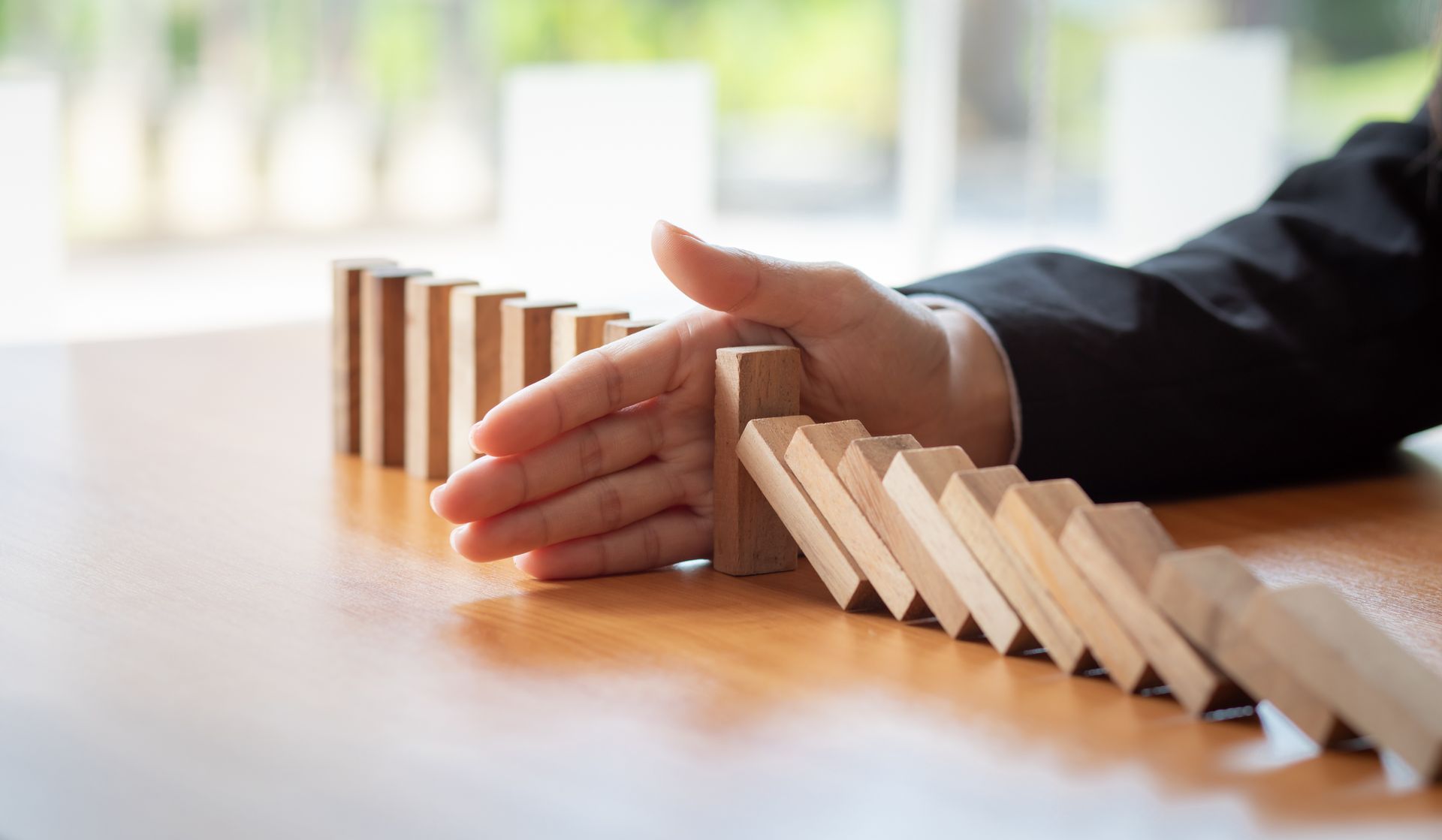 Hand stopping a row of falling dominoes on a table.