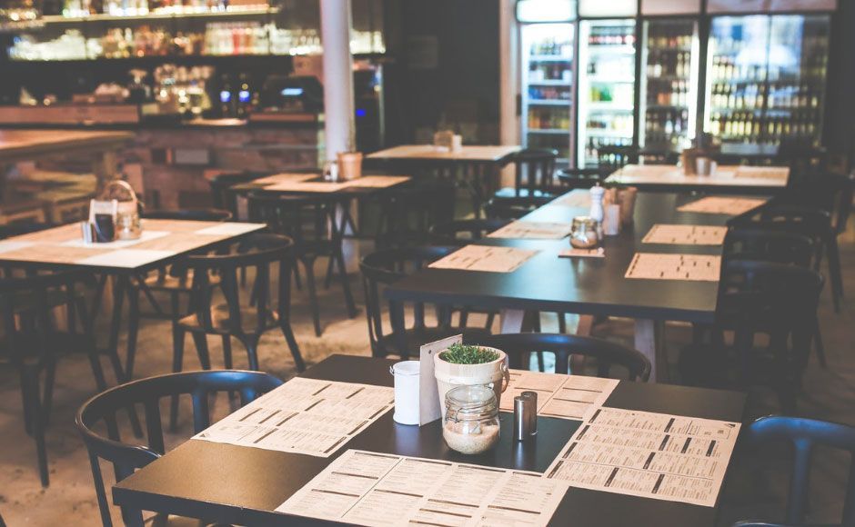 Empty restaurant interior with tables, chairs, and a bar in the background.