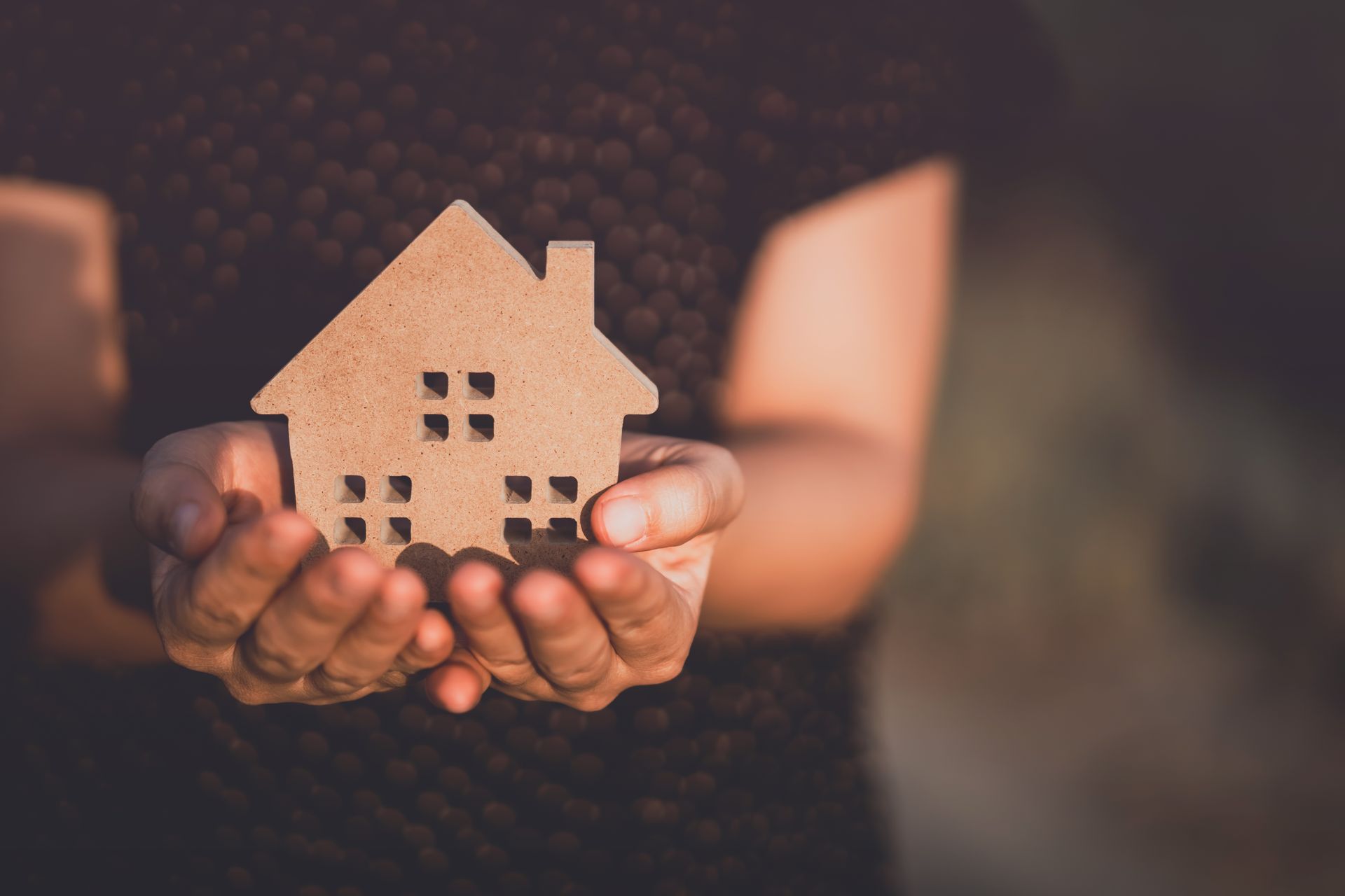 Hands holding a small, brown house cutout, symbolizing home or security.