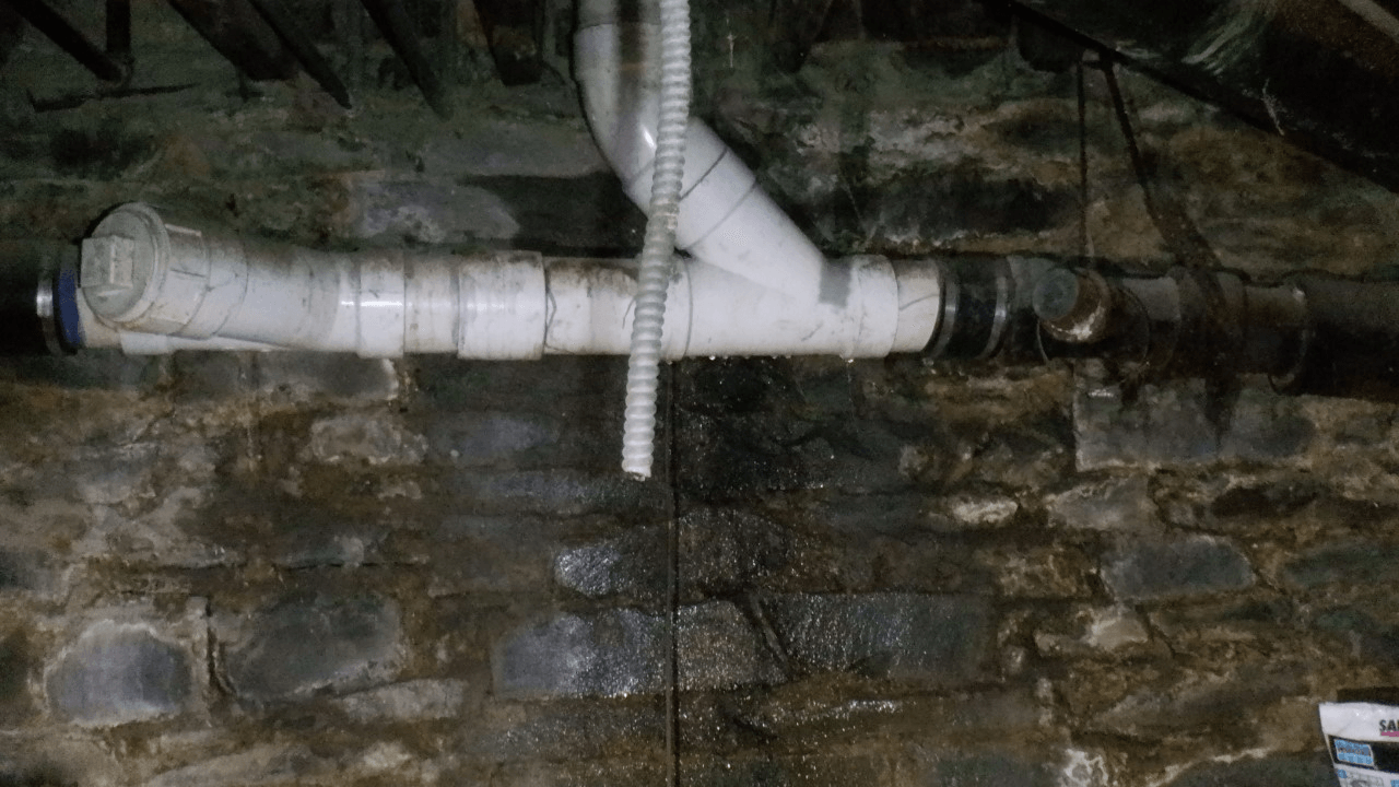 A white pipe is attached to a brick wall.