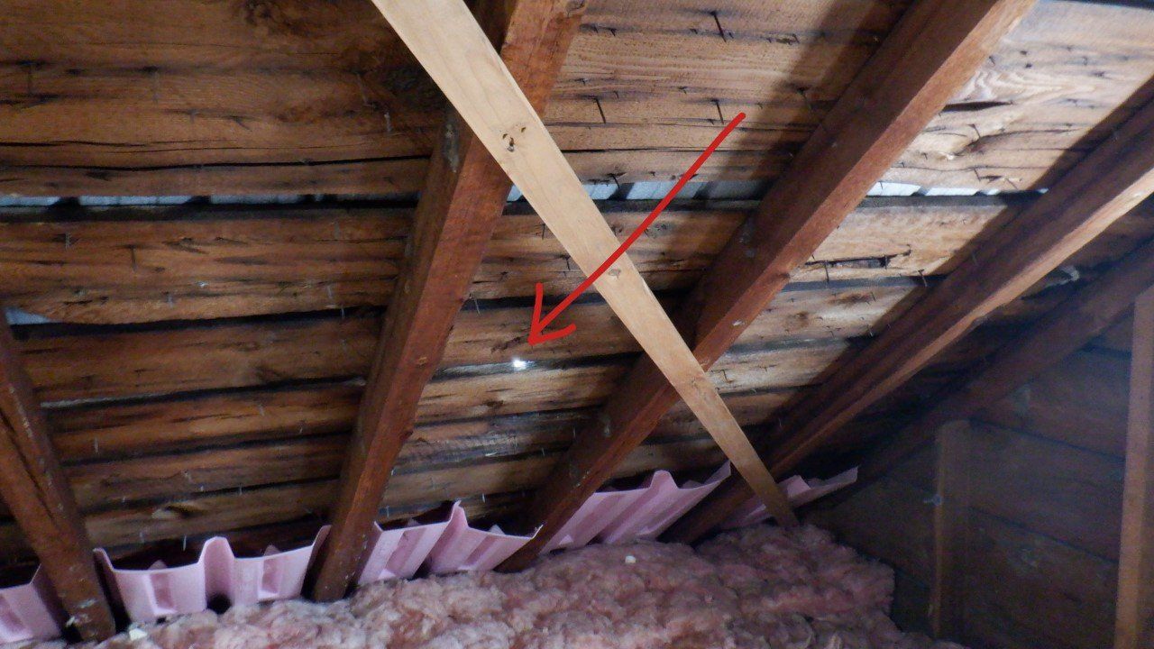 A red arrow points to a hole in the ceiling of an attic.