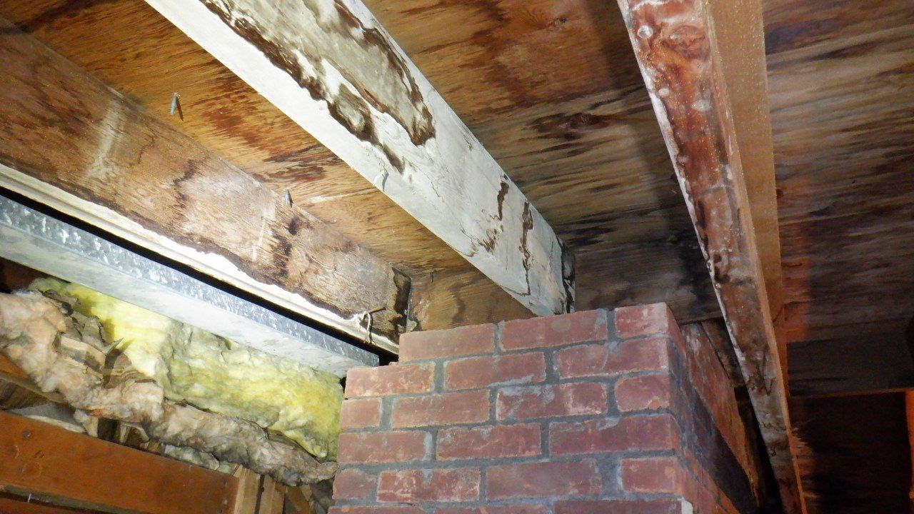 A brick chimney is sitting under a wooden ceiling in an attic.