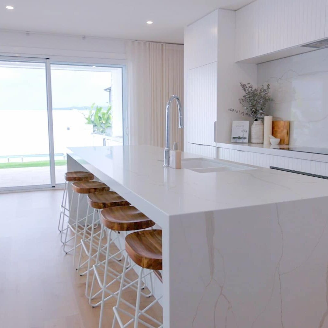 A Kitchen With a Long White Counter Top and Wooden Stools — Evolution Building Group Dapto, NSW