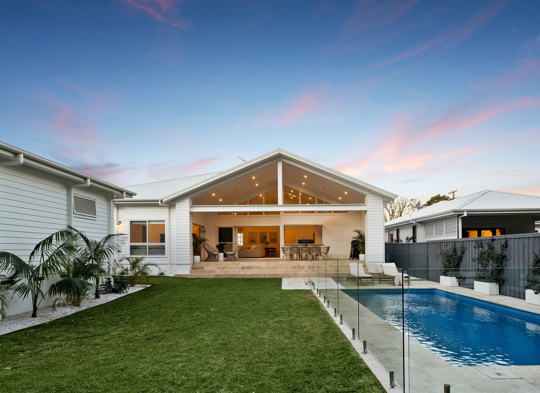 Backyard View of a White House With a Pool, Lawn, and Open Living Area With an Evening Sky — Evolution Building Group in Dapto, NSW