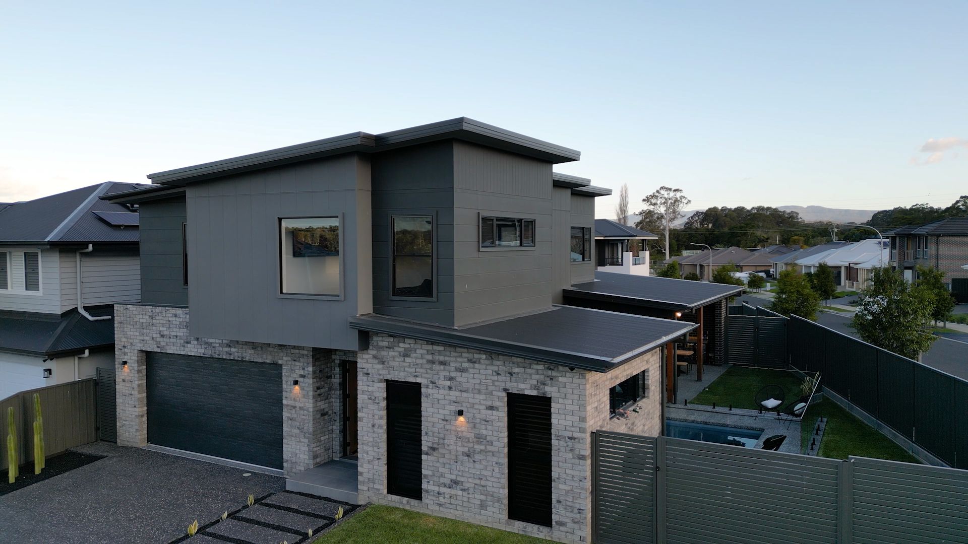 Modern two-story house with grey and light brick exterior. Features a garage, small windows, and a black fence — Evolution Building Group In Appin, NSW