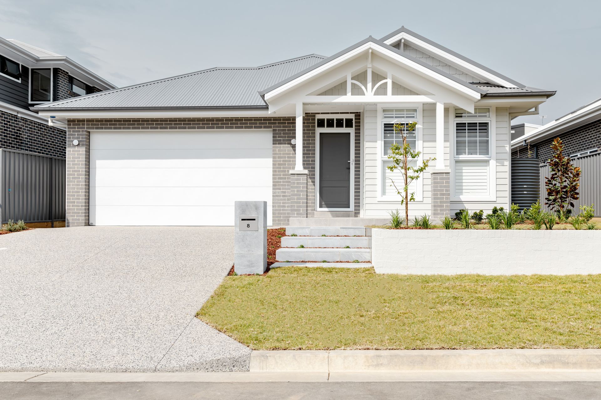 A modern, single-story house with a grey roof, white exterior, and a gravel driveway. A mailbox stands in front of the small lawn — Evolution Building Group Dapto, NSW