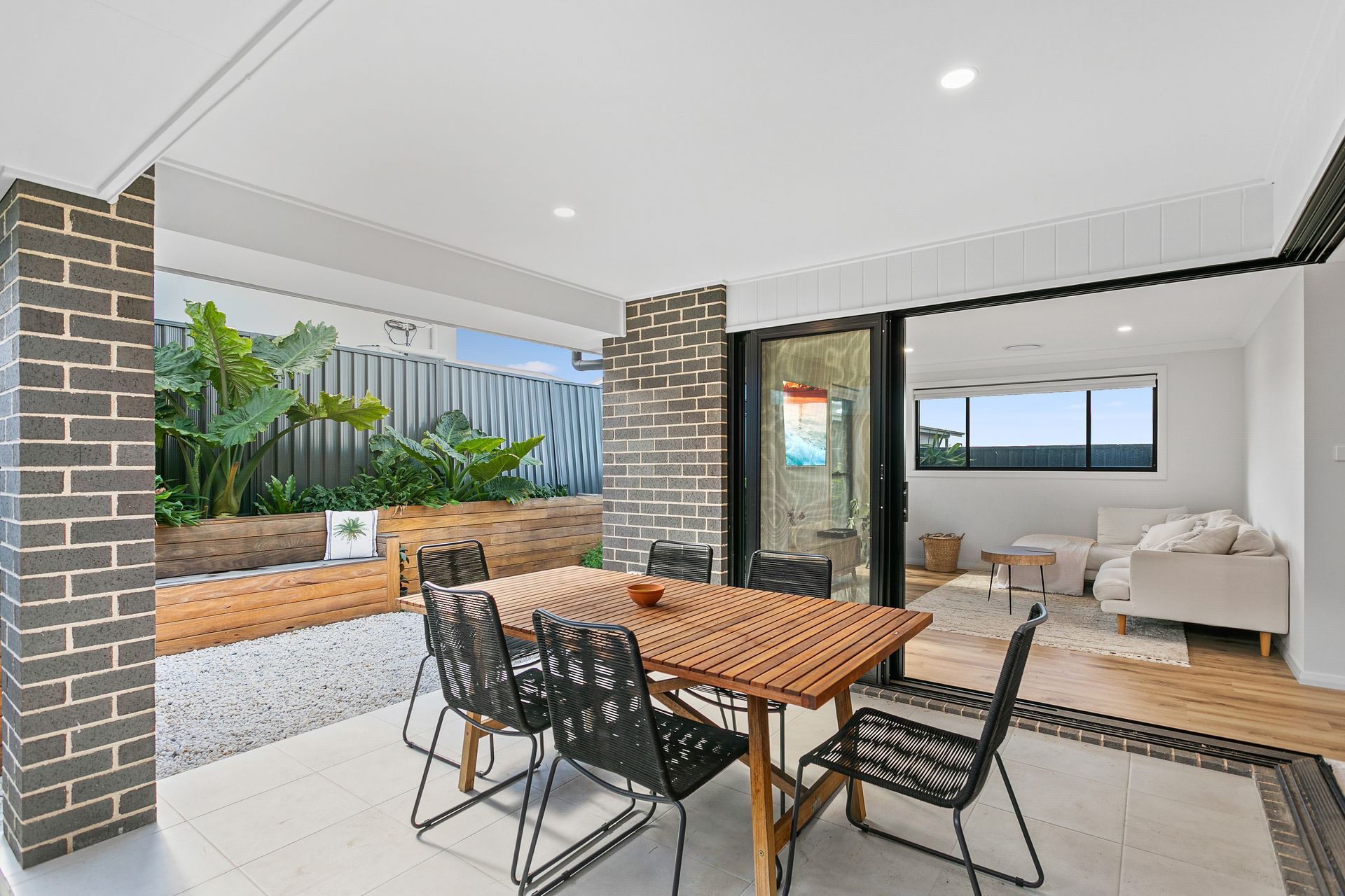 An outdoor dining area with a wooden table and black chairs under a covered patio, connected to a living room — Evolution Building Group In Moss Vale, NSW