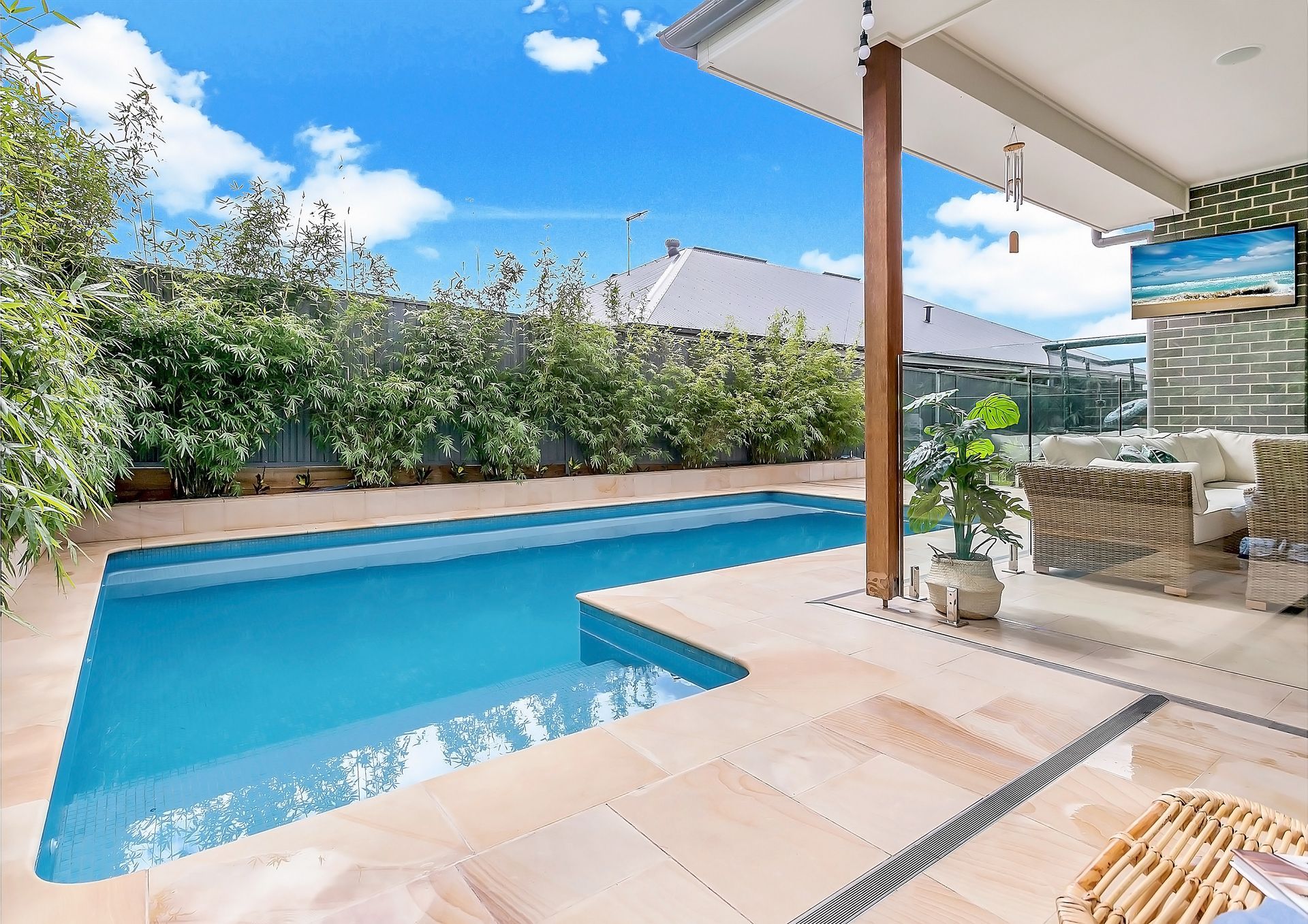 Pool and patio area with blue water, tan tiles, and a lush green fence under a bright blue sky — Evolution Building Group Dapto, NSW