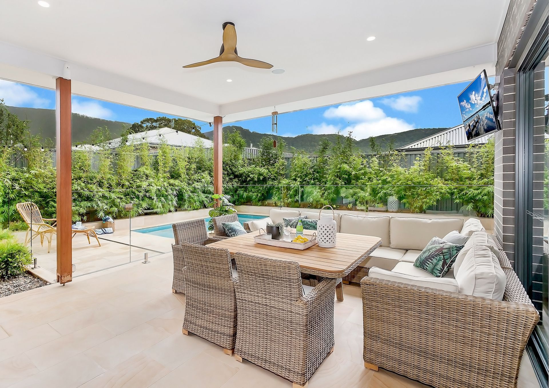 Outdoor patio with wicker furniture, a dining table, and a pool in the background, under a light-coloured roof with a mountain view — Evolution Building Group In Shoalhaven, NSW