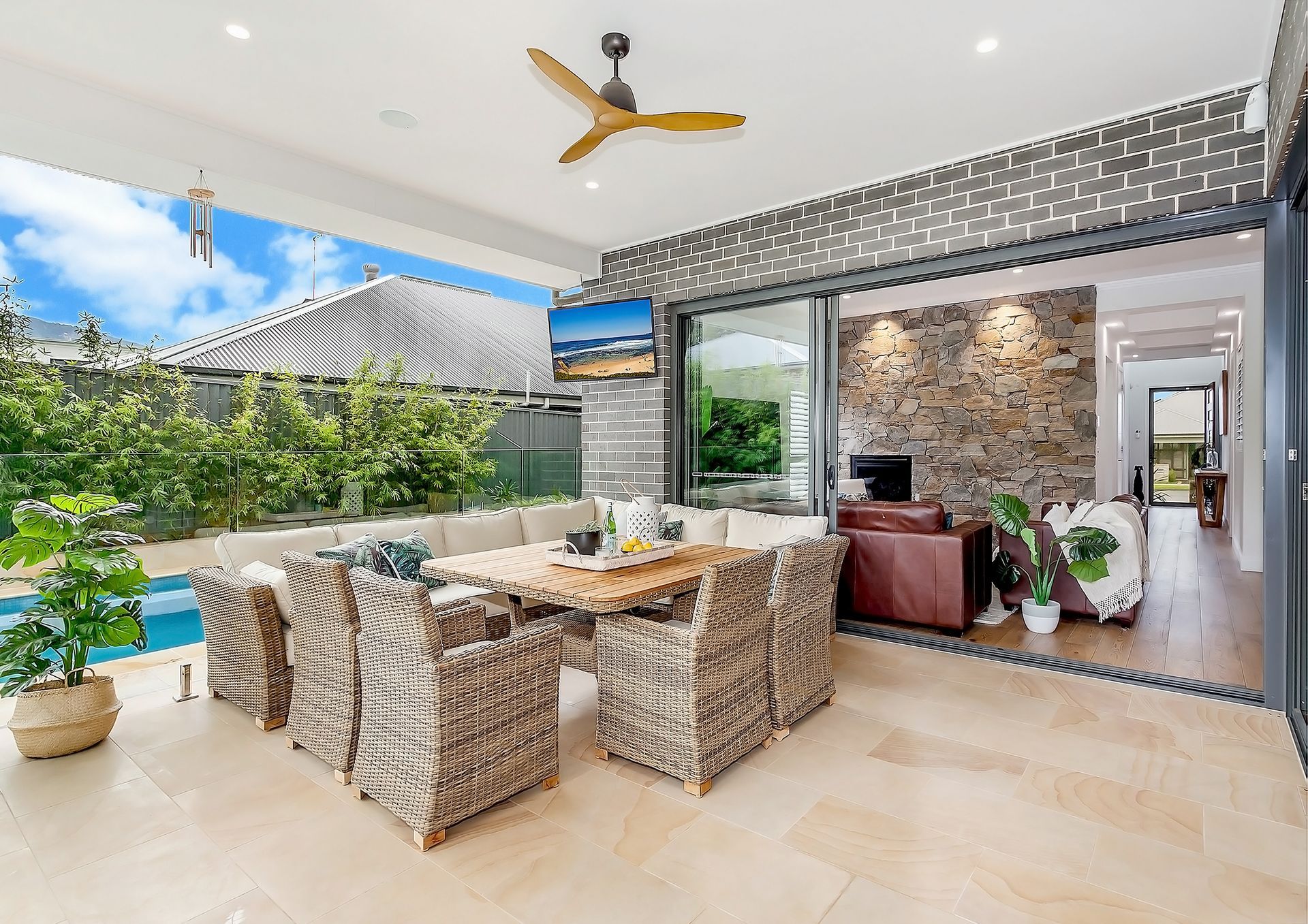 Outdoor patio with wicker furniture, a dining table, and a pool view. A television is mounted on a stone wall — Evolution Building Group In Gerringong, NSW