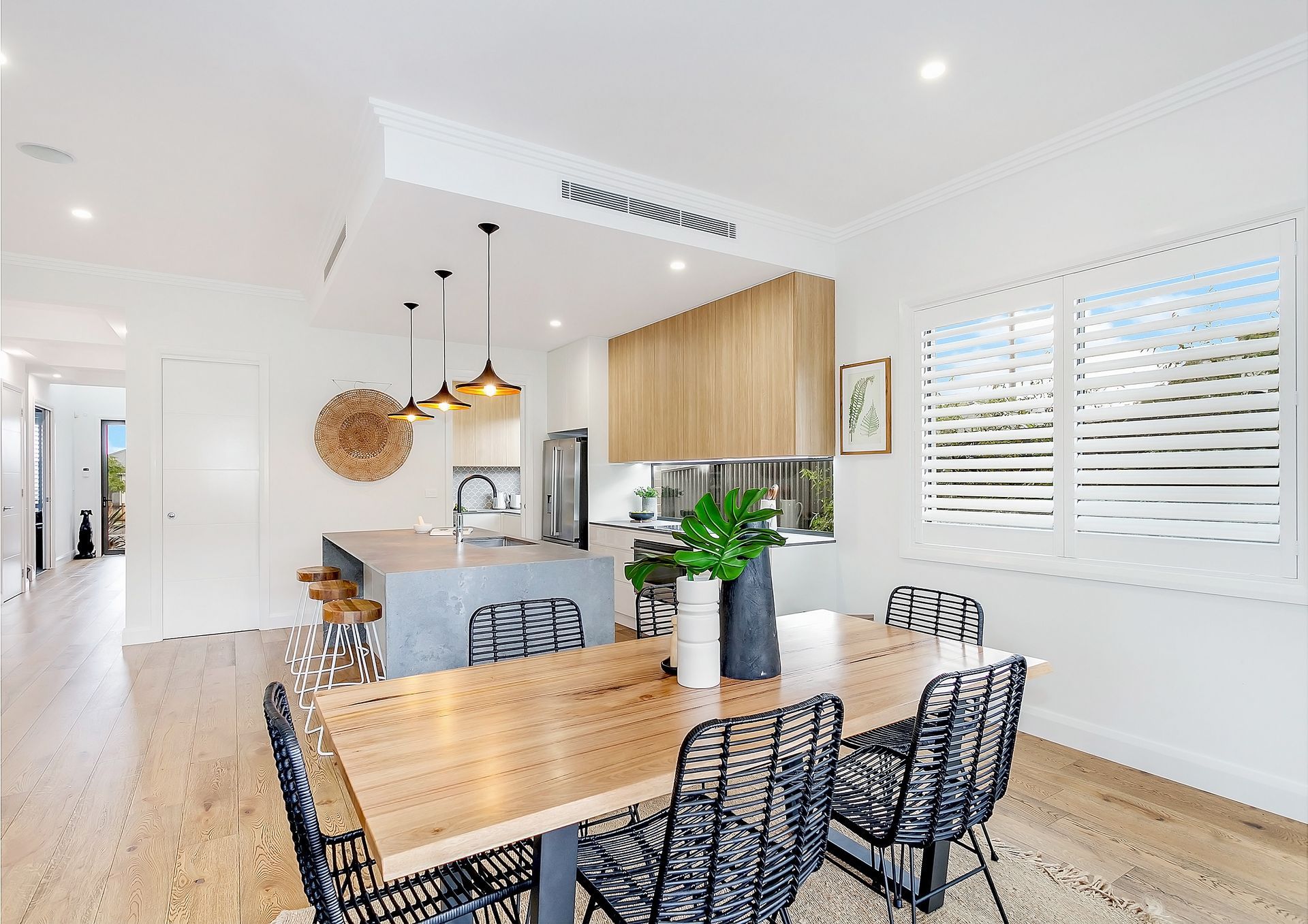 Open-concept dining and kitchen area with light wood flooring, a wooden table with black chairs, and a grey island with stools — Evolution Building Group In Southern Heights, NSW