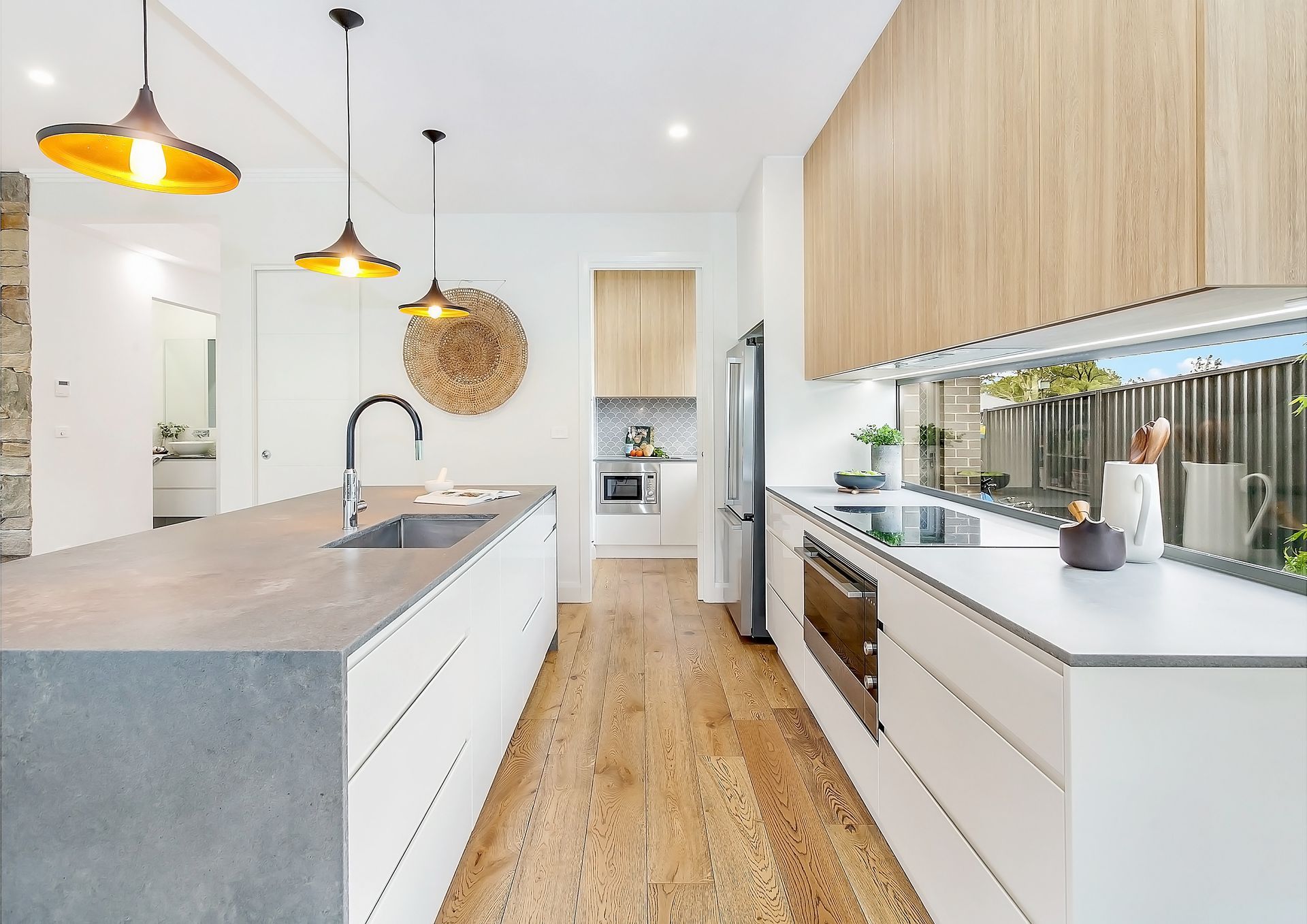 Modern kitchen with white cabinetry, a concrete island, and a wood floor. Overhead pendant lights and a large window with a view — Evolution Building Group In Woonona, NSW