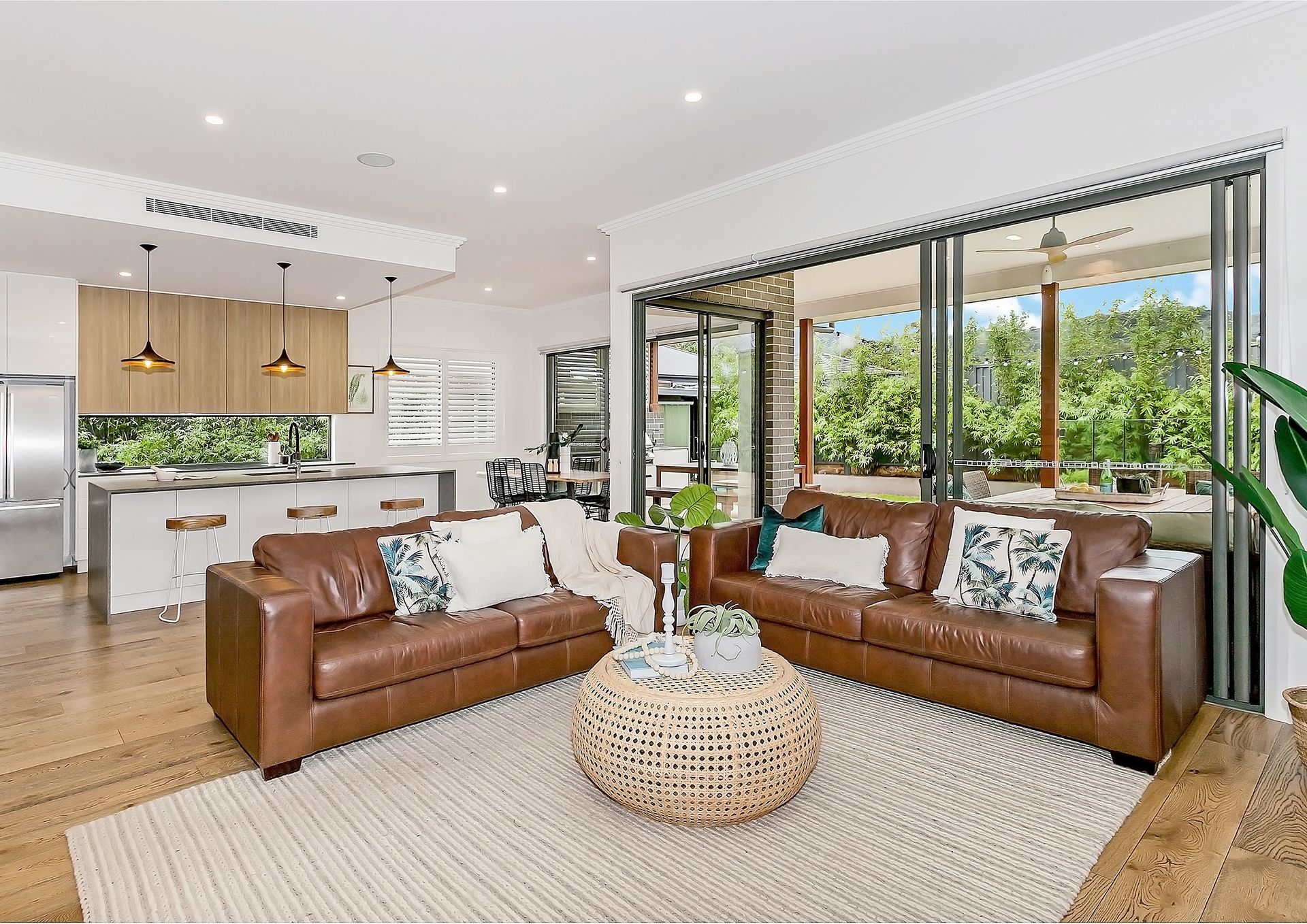 A spacious living room with two brown leather sofas, a woven coffee table, and a view of a lush outdoor area — Evolution Building Group In Bowral, NSW