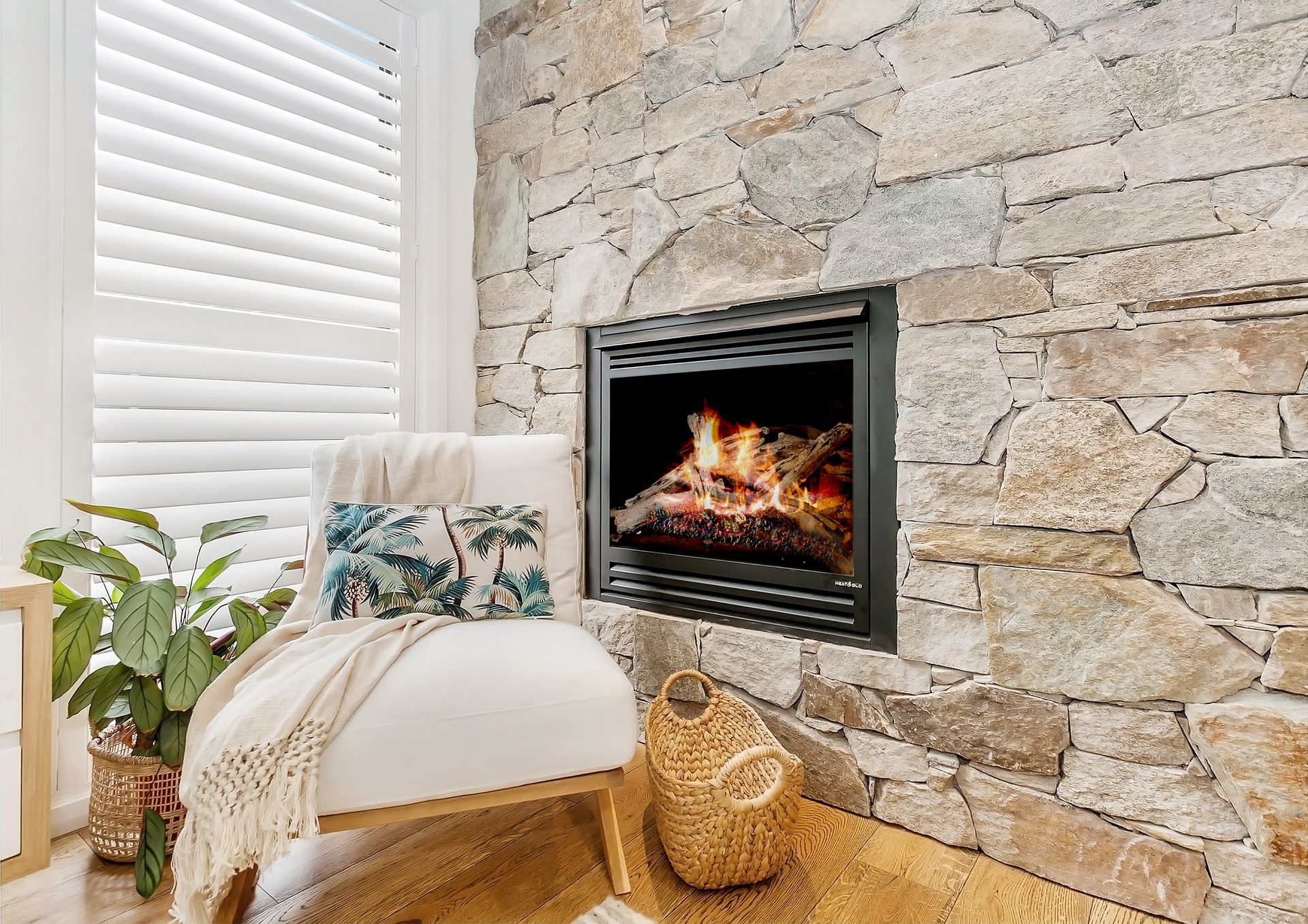 Cozy living room with stone fireplace, lit flames, armchair, shutters, and plants — Evolution Building Group In Southern Heights, NSW