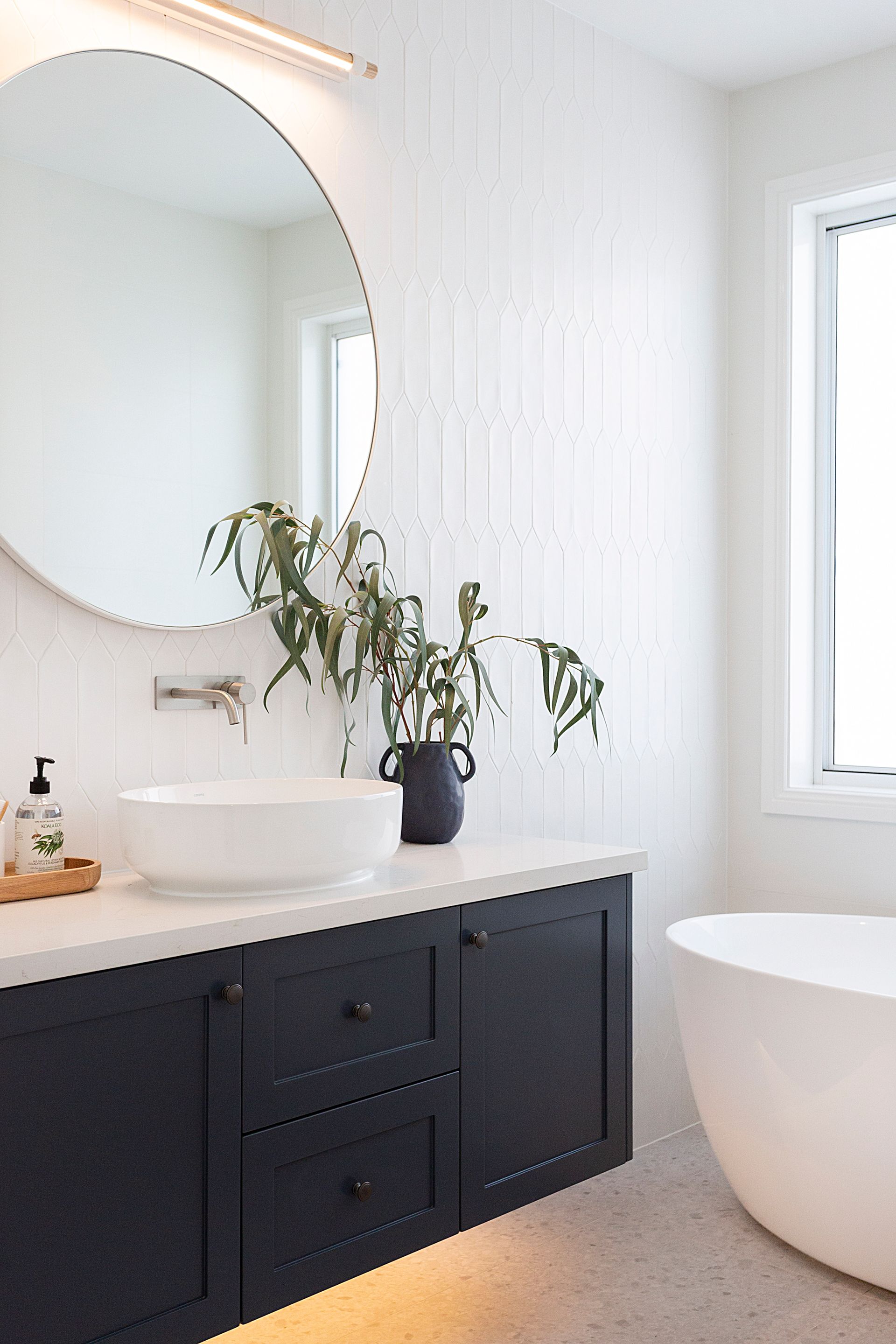 Modern white bathroom with a black vanity, round mirror, and a freestanding bathtub — Evolution Building Group Dapto, NSW