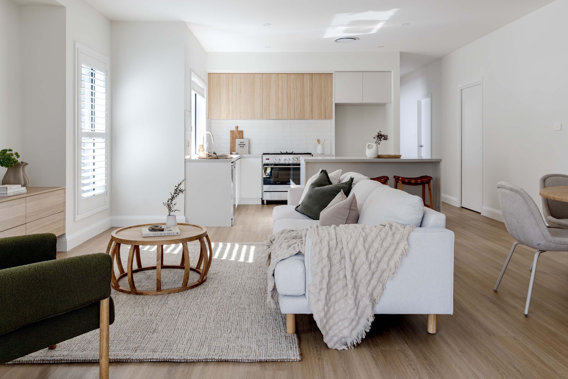 A modern living room with a white couch, wood accents, and an open kitchen in the background. Sunlight streams through a window — Evolution Building Group Dapto, NSW