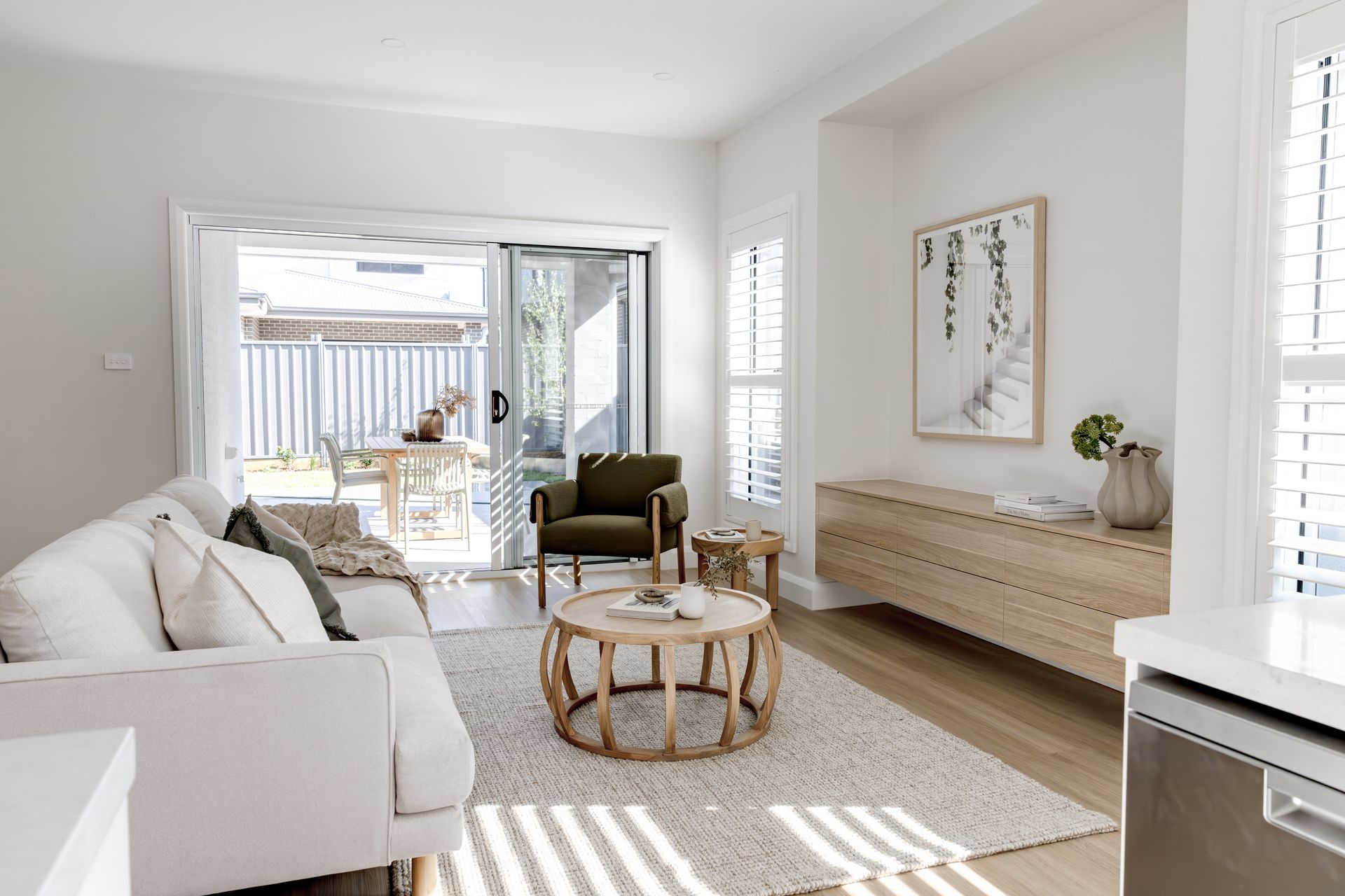 Bright living room with a white sofa, olive green armchair, and sliding glass door to a backyard patio. Wooden coffee table and storage cabinet — Evolution Building Group In Southern Heights, NSW