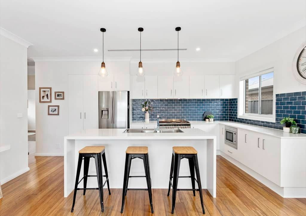 A Kitchen With White Cabinets, Stools, a Refrigerator and a Clock on the Wall — Evolution Building Group Dapto, NSW