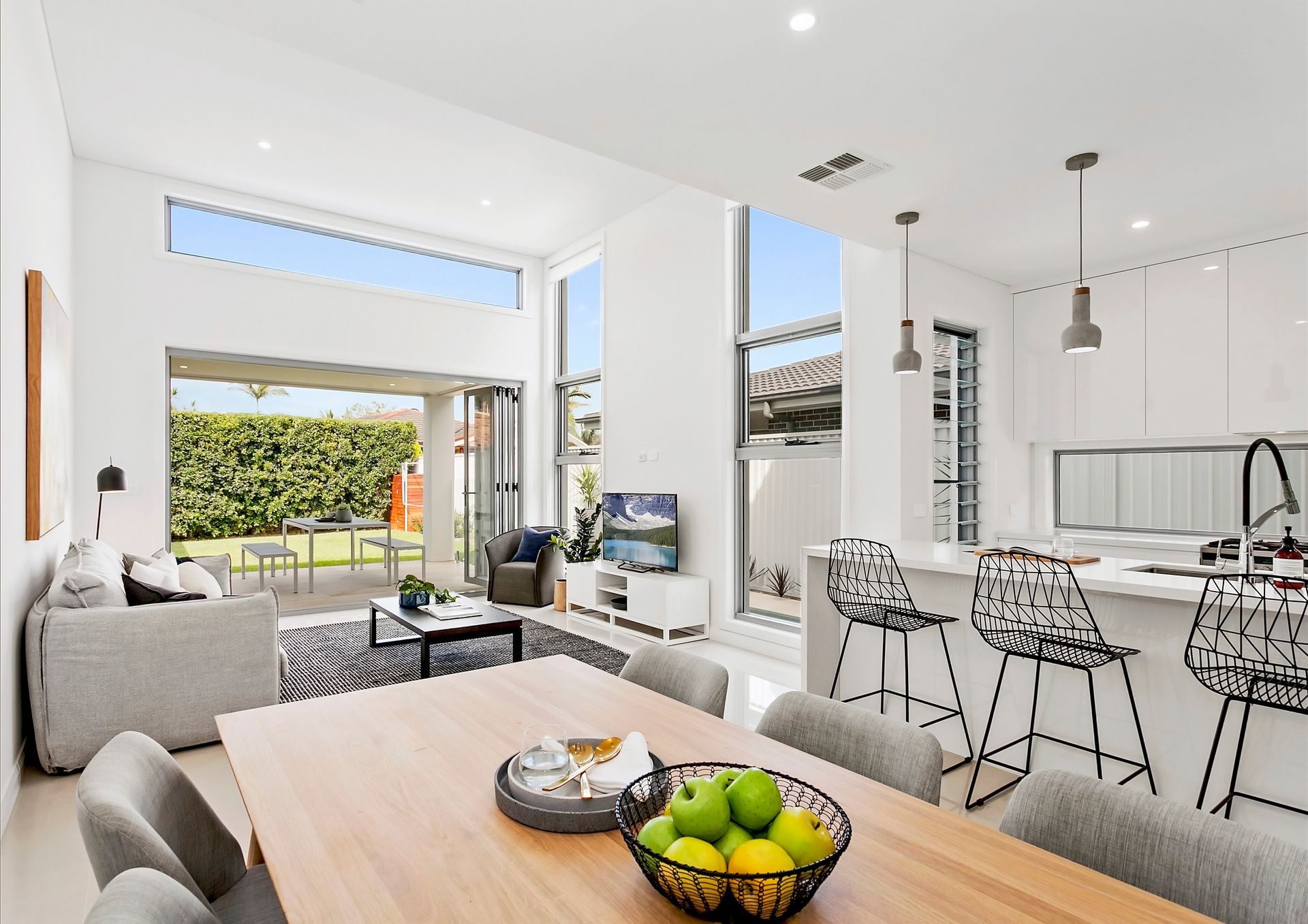 A bright, modern living space with a dining area, open kitchen, and access to an outdoor patio with lush greenery — Evolution Building Group In Woonona, NSW
