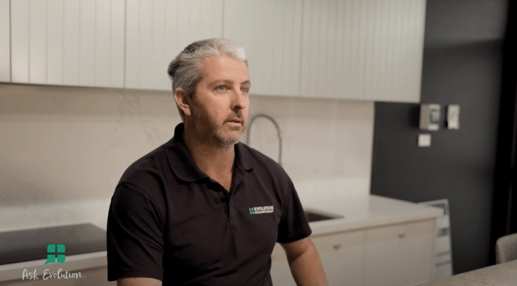A Man in a Black Shirt is Sitting in a Kitchen — Evolution Building Group Dapto, NSW