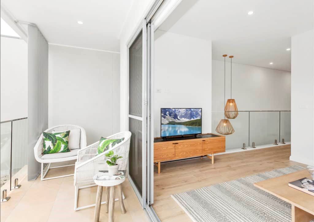 A modern living room with a balcony. White wicker chairs, wood console, TV, pendant lights, and wood flooring — Evolution Building Group Dapto, NSW