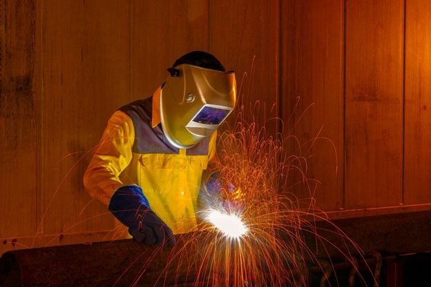 A man wearing a welding mask is welding a piece of metal.