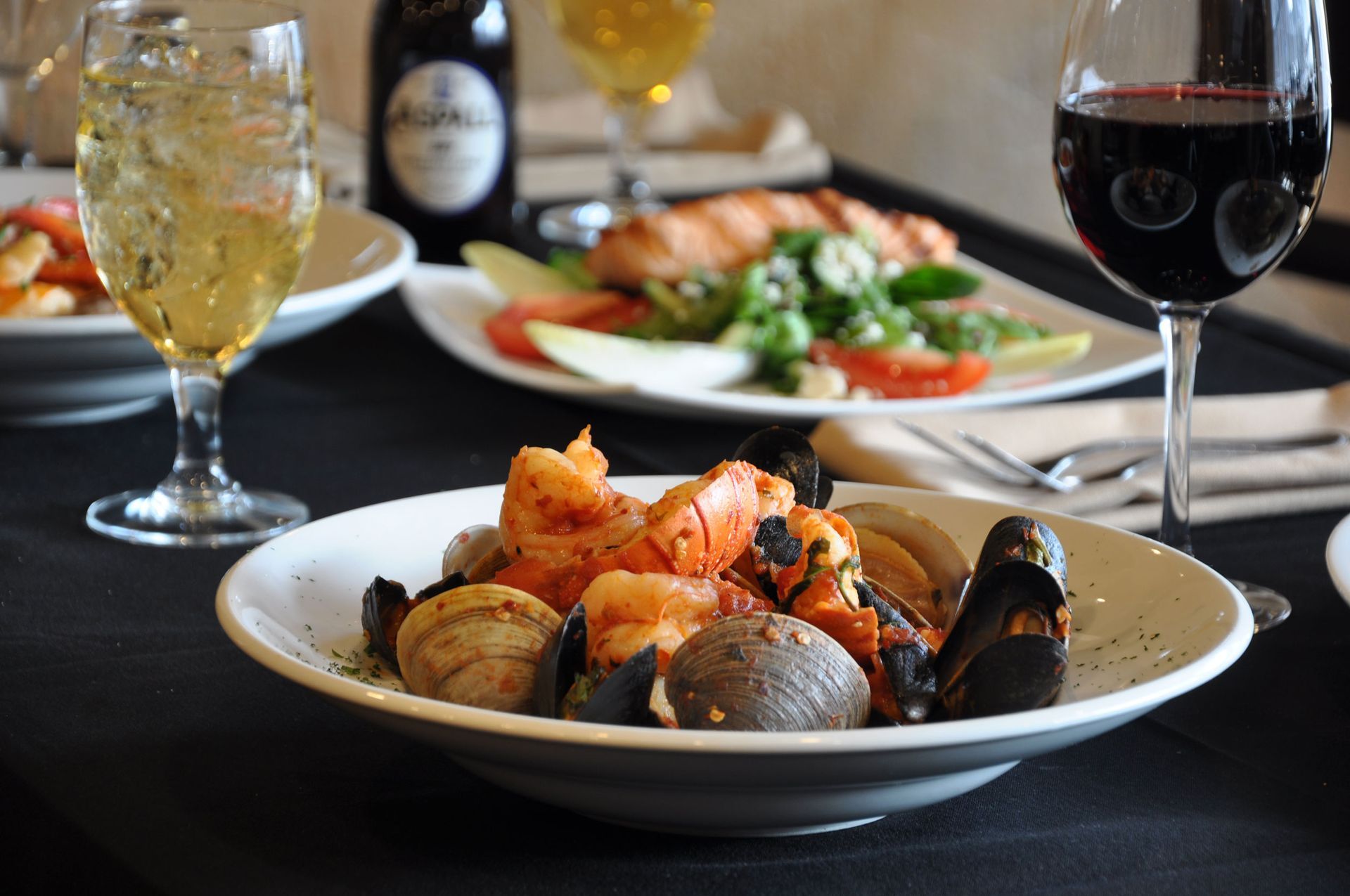 A bowl of seafood sits on a table next to a glass of wine