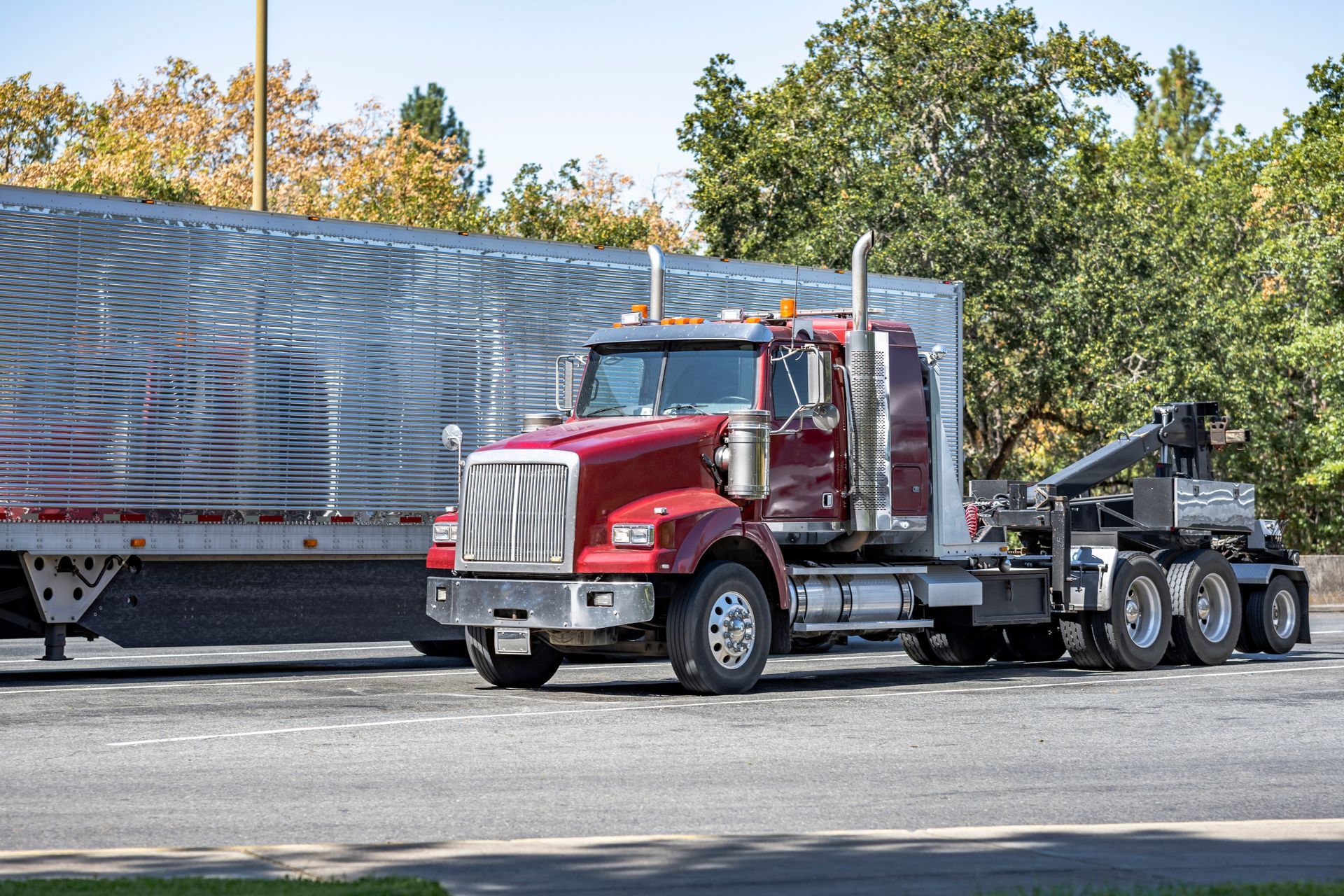 A red semi truck is towing a silver trailer down the road.
