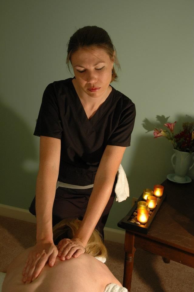 A woman is giving a massage to a woman in a room with candles on the table.
