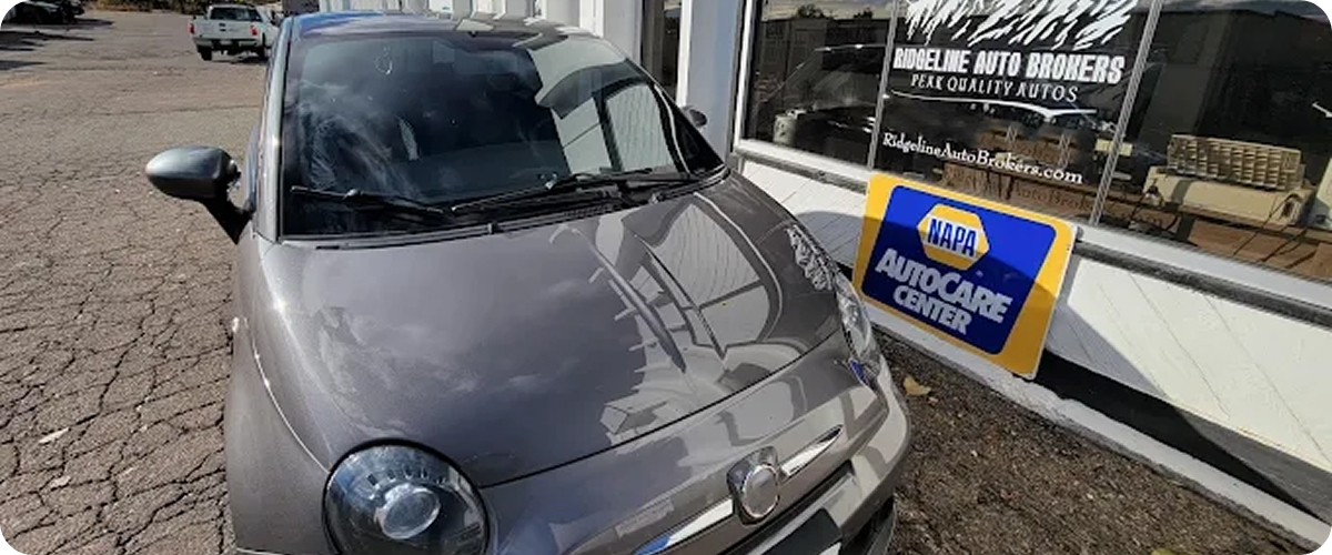 A gray car is parked in front of a car dealership. | Ridgeline Automotive