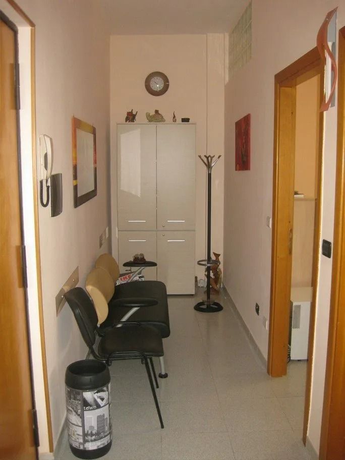 Narrow hallway with white cabinets, black chairs, and a coat rack. Pale pink walls, a clock, and a doorway are visible.