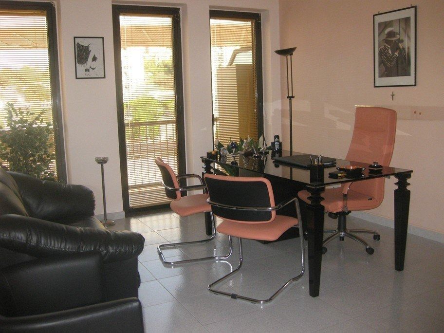 Office with black desk, peach chairs, black leather couch, and large windows.