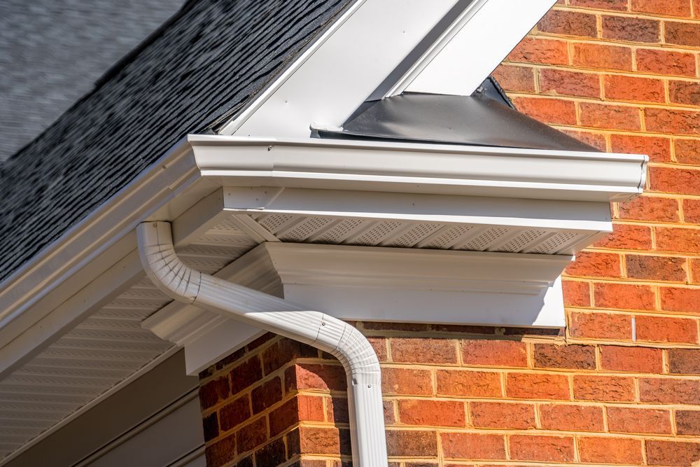 White gutter and downspout on a brick house beneath a gray roof eave