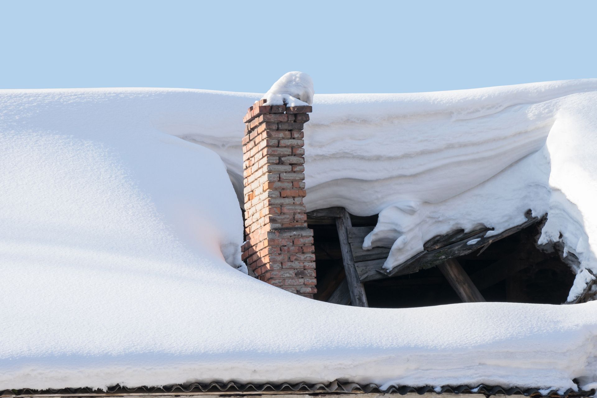 Brick chimney protruding from a snow-covered roof; blue sky.