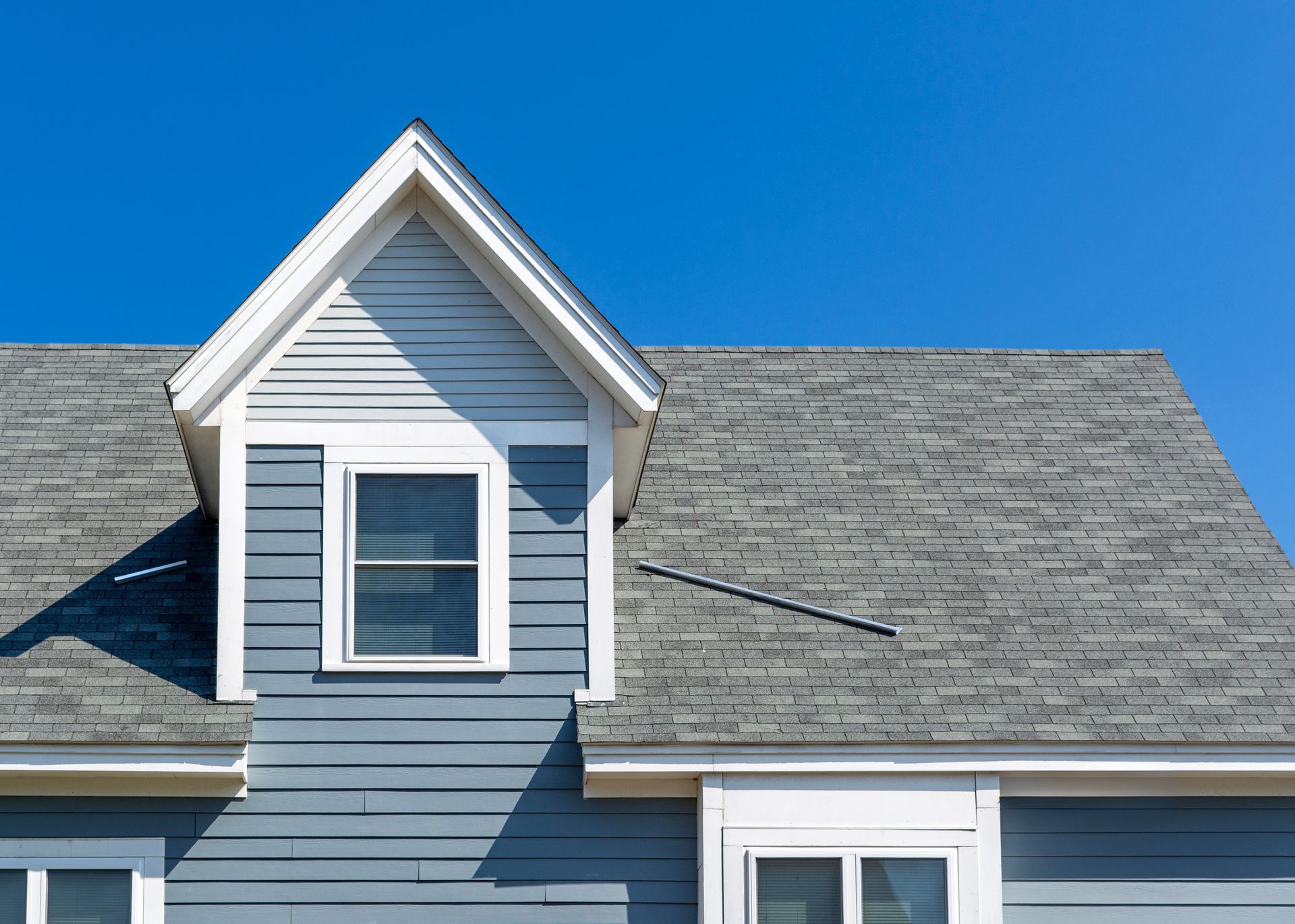 Blue house roof with a dormer and a bright blue sky.