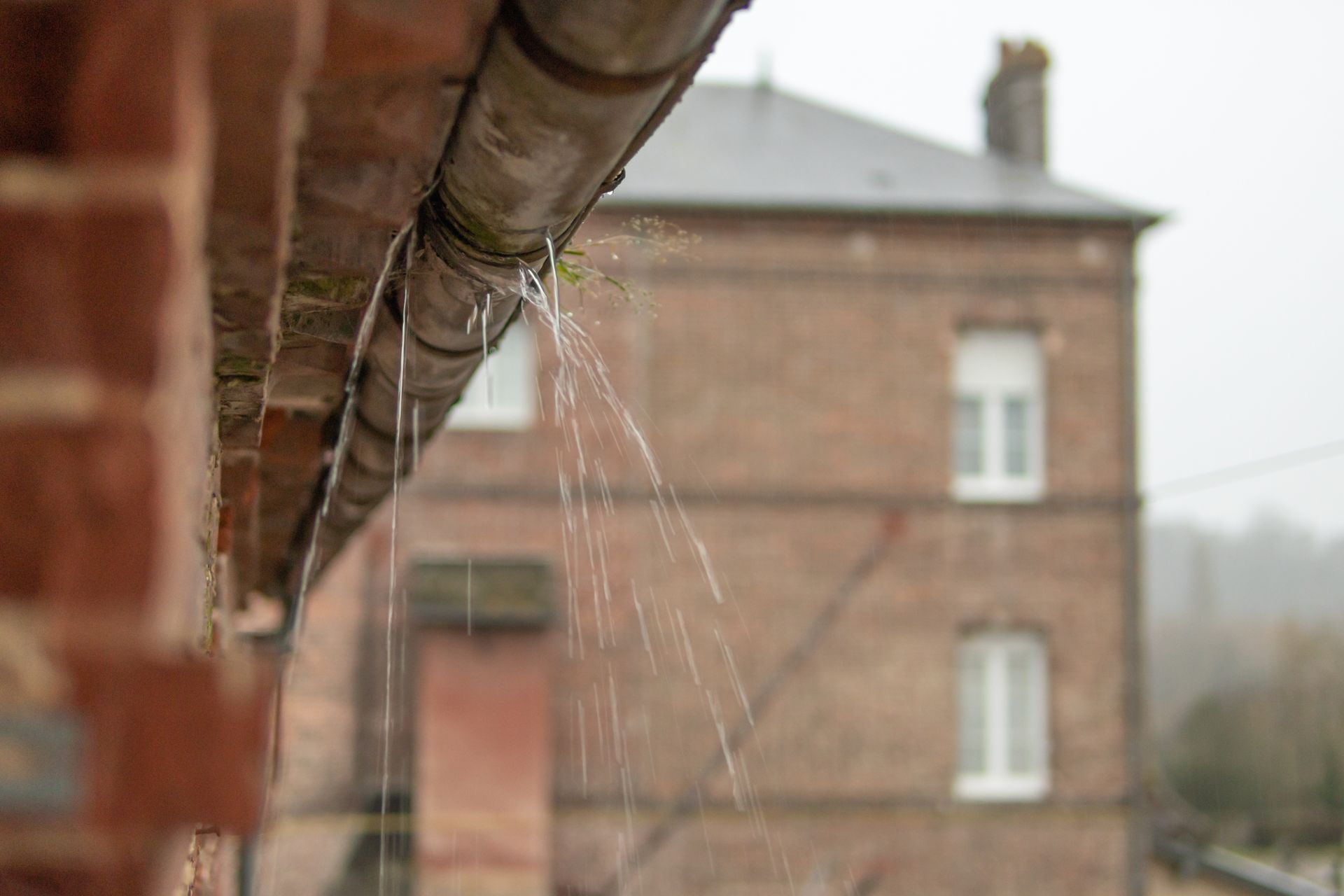 Rainwater splashing from a rusty gutter, in front of a brick building.
