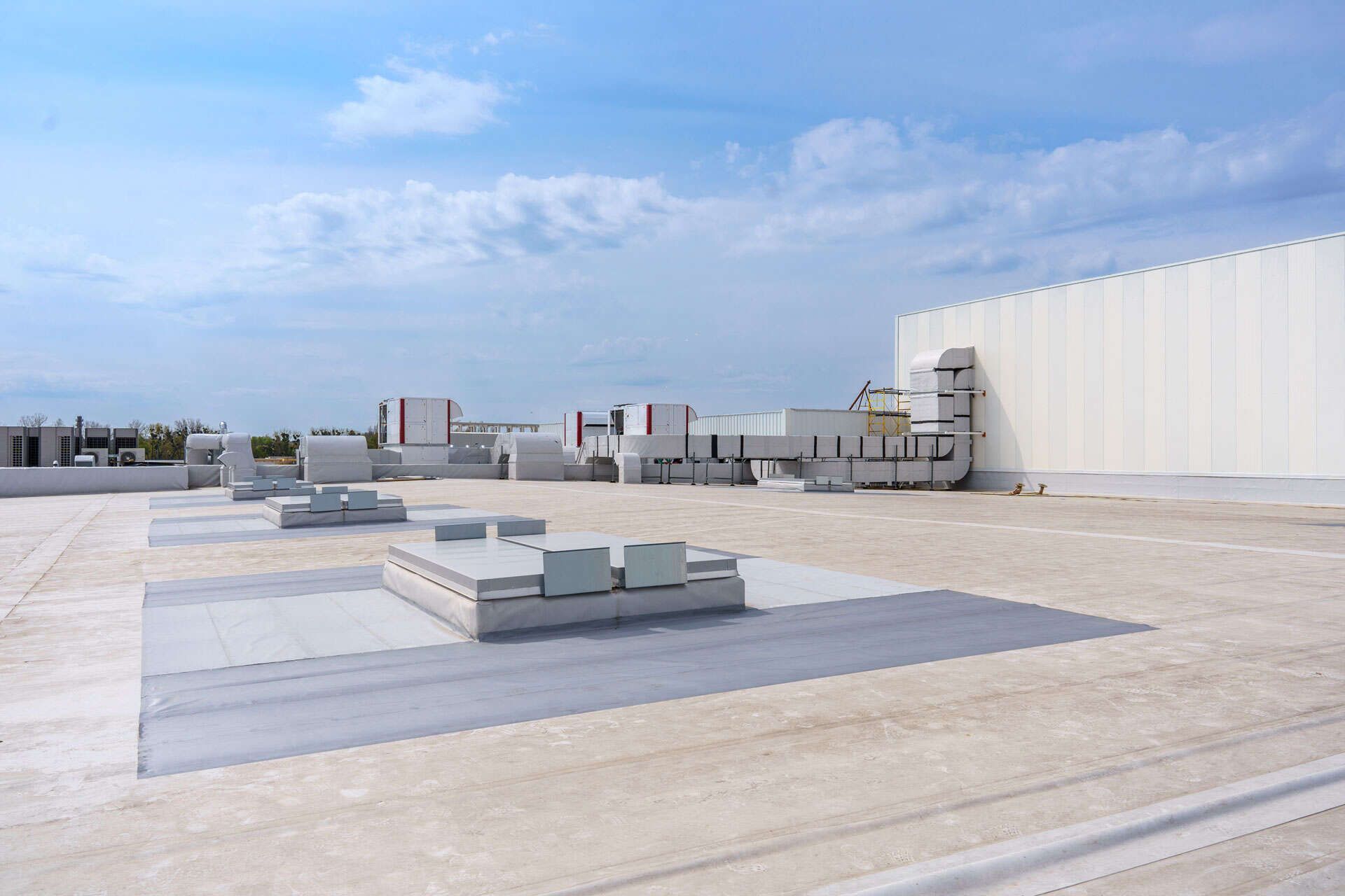 White flat roof with HVAC units under a cloudy sky.