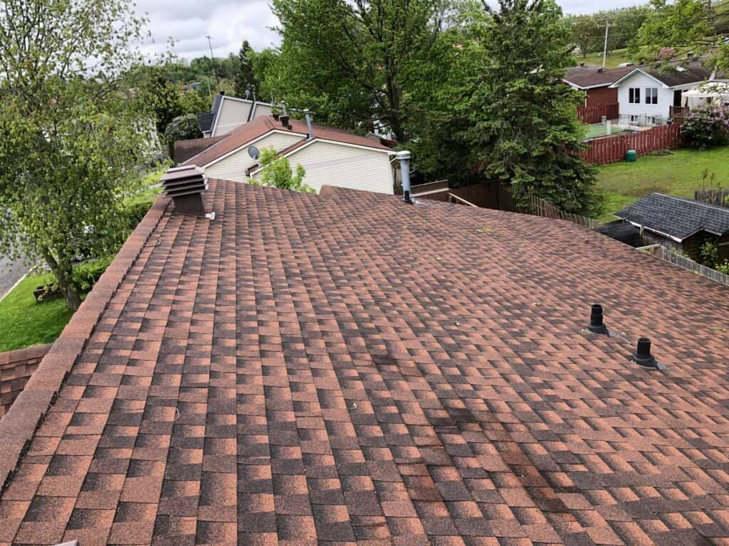 Brown shingled rooftop with a view of a street, trees, and houses on an overcast day.