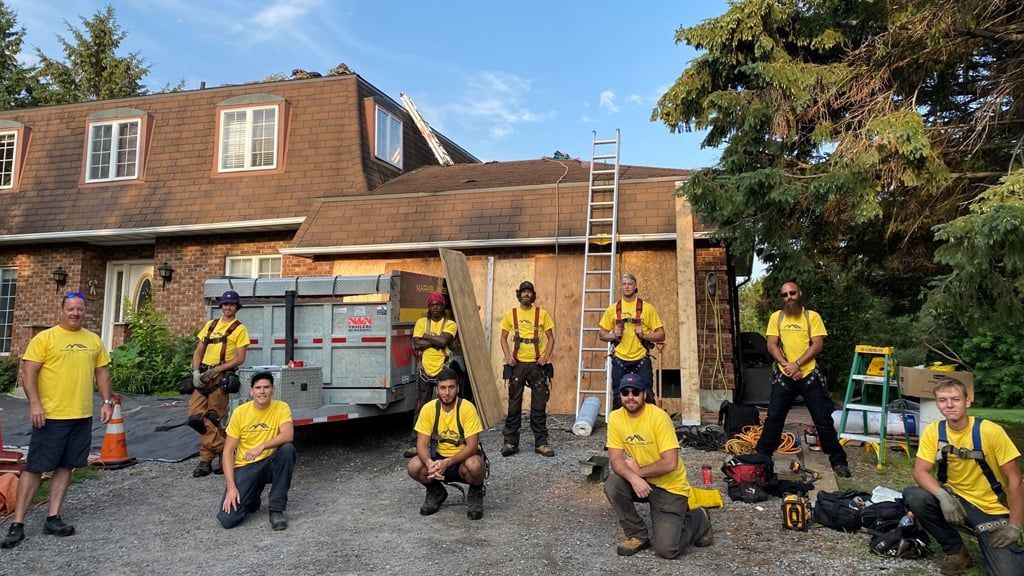 Roofing crew in yellow shirts and safety harnesses posing in front of a house under construction.