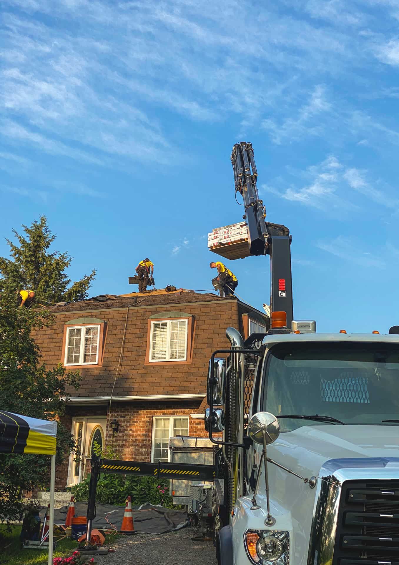 Construction workers on a roof, using a boom lift to place materials. Blue sky overhead.