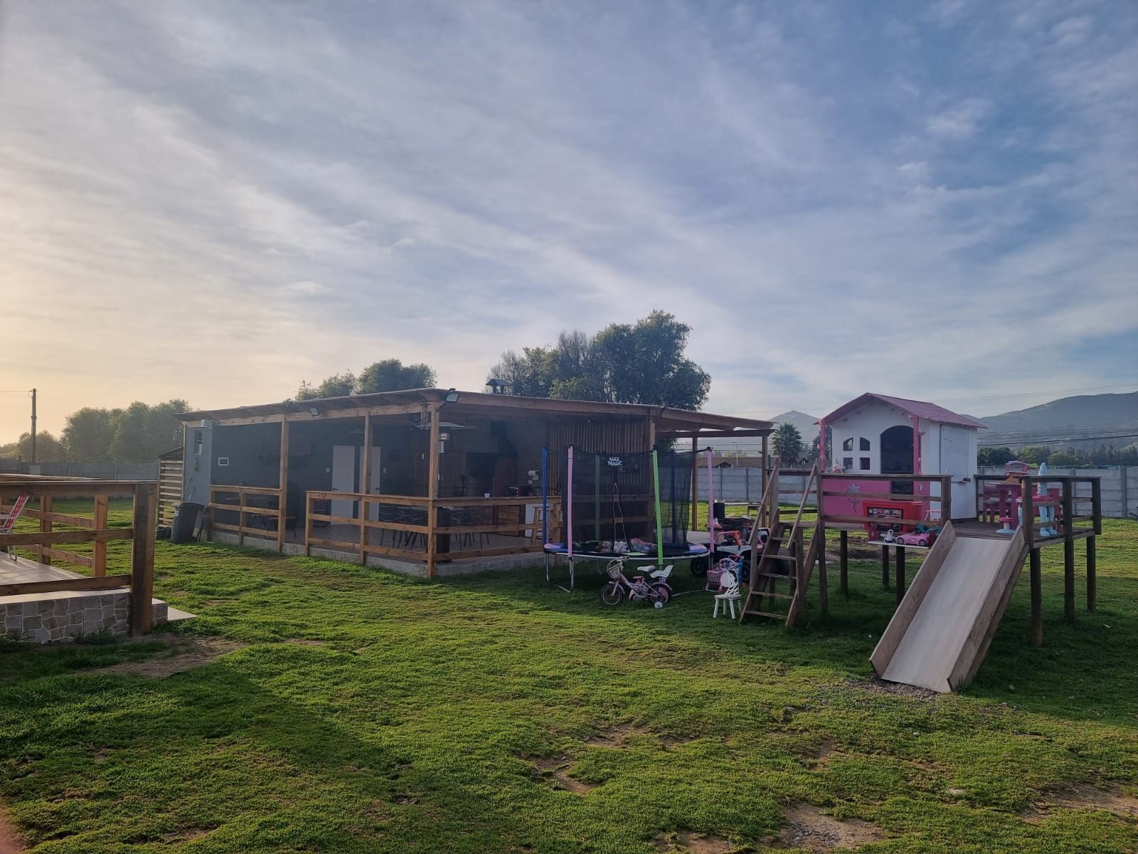 Un parque infantil con tobogán y una casa al fondo.