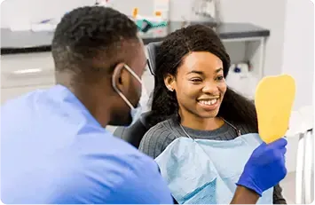 Dentist shows patient her teeth in a mirror. Both are smiling in a dental office.