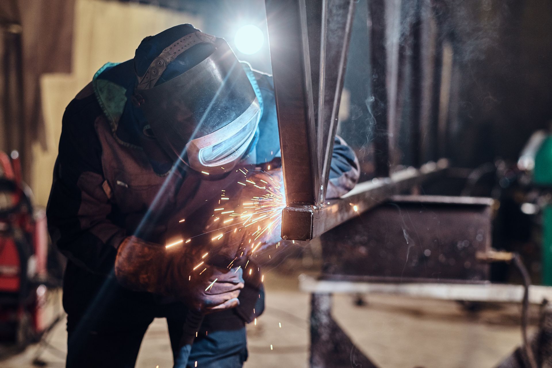Worker welding metal sparks in fabrication shop, protective gear and torch in action.