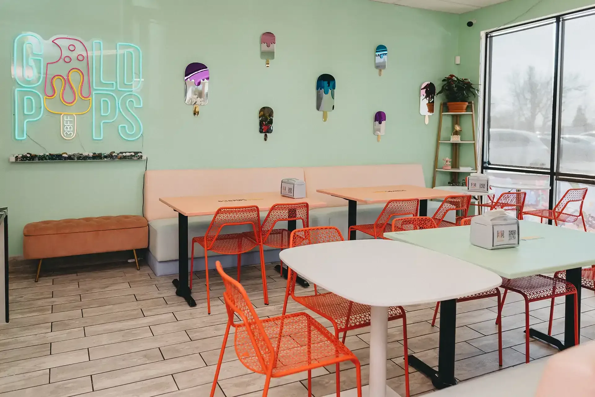 A dining room with tables and chairs and a neon sign that says gold pops.